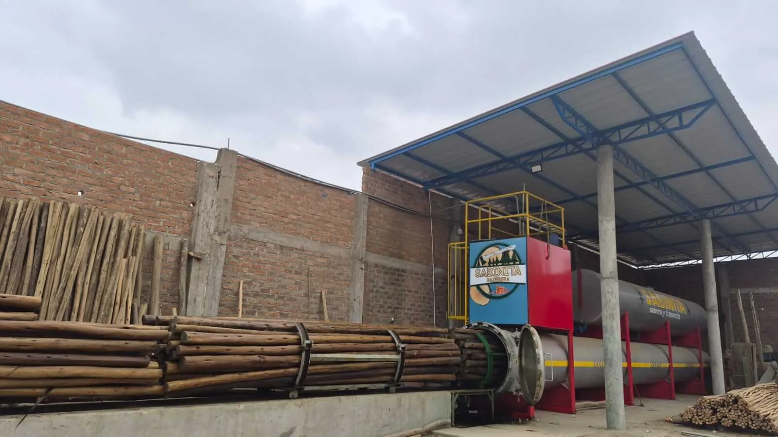 Almacén techado de Sabinita con postes de madera tratada apilados y maquinaria de carga